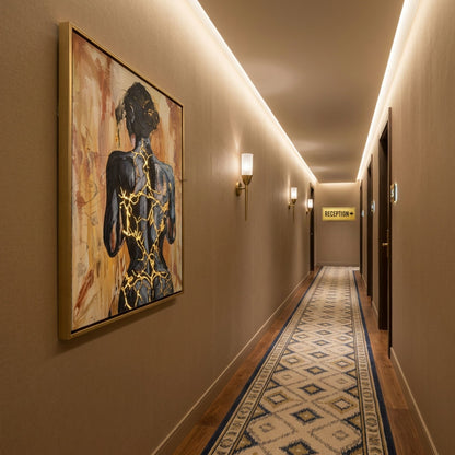 „Fortress Of Light“ von Marika Junikajtes als digitale Raumvisualisierung in einem warm beleuchteten Boutique-Hotel-Flur mit braunen Wänden, Holzfußboden und Messingleuchten. Das 60 × 80 cm große Originalgemälde zeigt eine dunkle Rückenfigur mit markanten goldenen Linien.