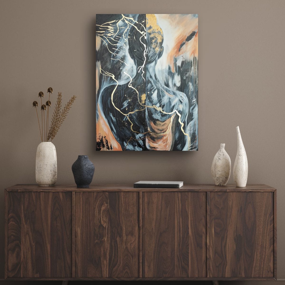 „Golden Burden“ über einem dunklen Holz-Sideboard in einem reduziert eingerichteten Raum mit brauner Wand und keramischen Objekten. Das Originalgemälde von Marika Junikajtes wirkt als ruhiger visueller Mittelpunkt.